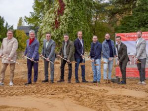 Gruppe bei Spatenstich für Seniorenresidenz, grüner Hintergrund, nachhaltiges Bauen, Herbst.
