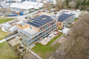 Luftaufnahme eines modernen Gebäudekomplexes mit Solaranlagen und begrüntem Außenbereich.