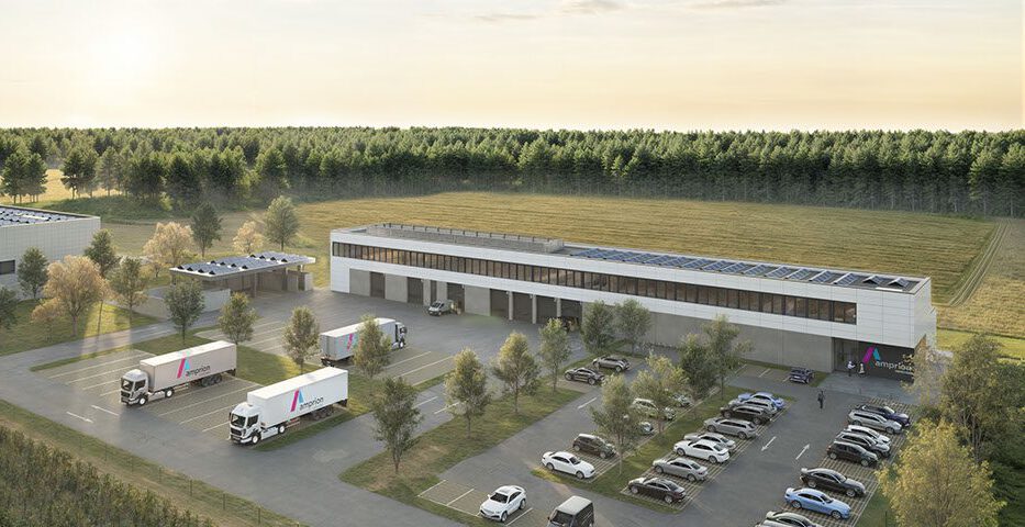 Moderne Logistikzentrale mit Lkw, Solarzellen und Parkplätzen, umgeben von Wald und Feldern unter bewölktem Himmel.